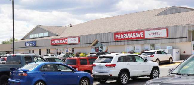 Multiple cars parked in large parking lot out front of a large building with Pharmasave Ahmerst signage