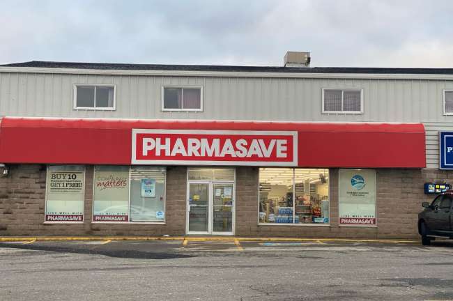 Exterior of pharmacy retail store with Pharmasave signage and four empty parking spots out front, one of which is marked as accessible