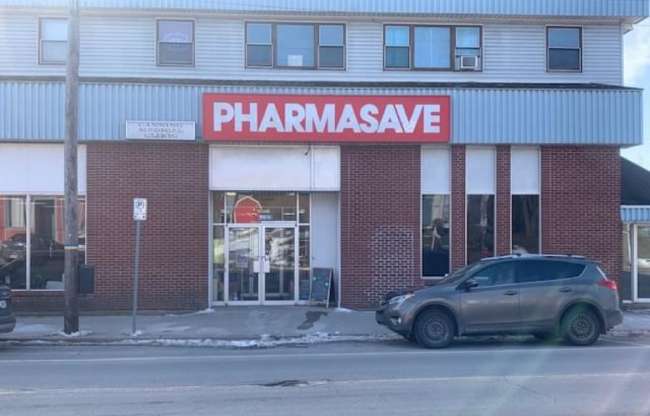 Exterior building of a Pharmasave store with a black SUV parked on the street