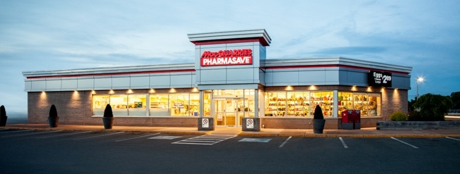 Large retail store exterior lit up at dusk with Macquarries Pharmasave signage and multiple empty parking spots