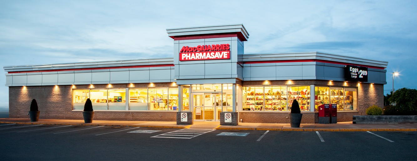 Large retail store exterior lit up at dusk with Macquarries Pharmasave signage and multiple empty parking spots