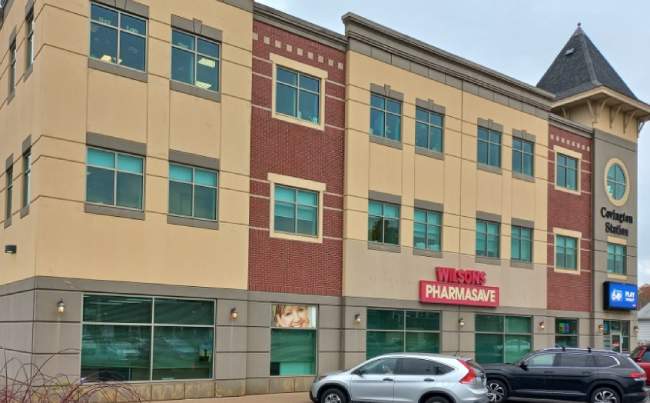 an brown-and-beige building with cars parked in front of it and a Pharmasve store sign