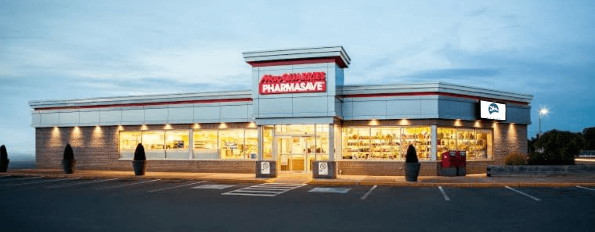 Large retail store exterior lit up at dusk with Macquarries Pharmasave signage and multiple empty parking spots