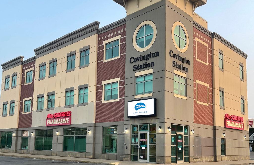 Covington Station building featuring MacQuarries Pharmasave storefront with modern brick and beige architecture, multiple stories, and street-level retail space.